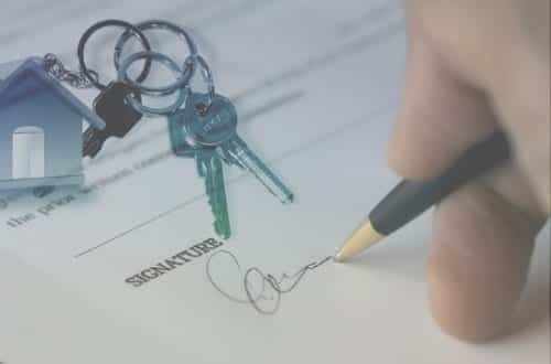 A hand signing a document with a bunch of keys attached to a little house key chain.