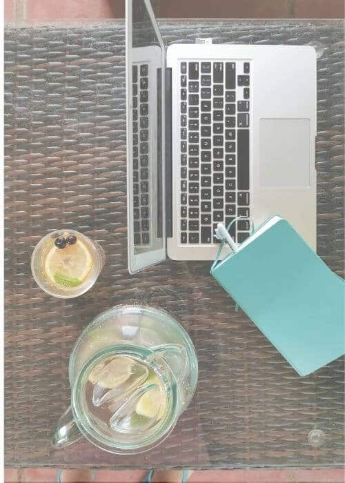 View from above onto a table with a laptop, notebook and a pitcher of water with a glass nearby.