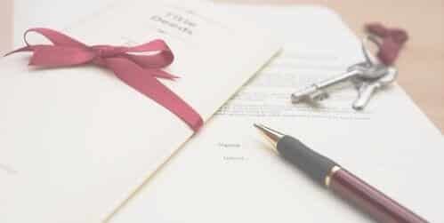 Documents on a table with a set of keys and a pen. Folded documents have a red ribbon around.